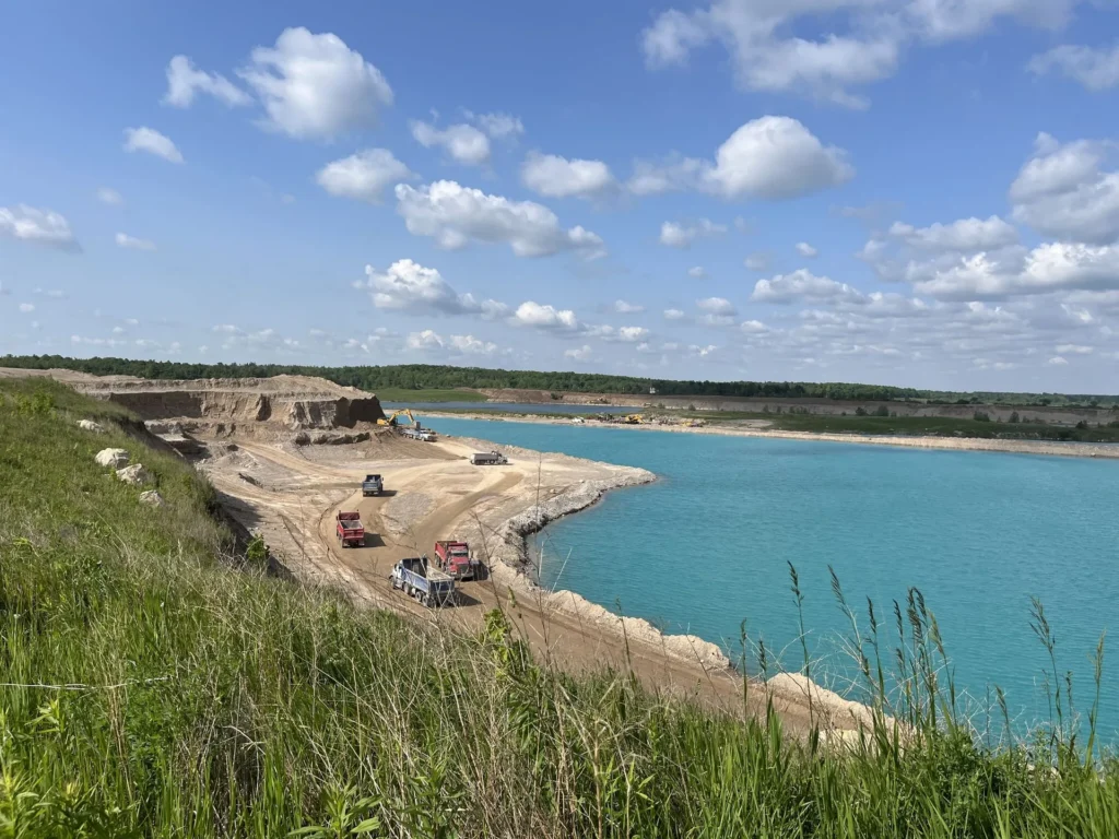 Dump trucks and an excavator working a sand and gravel pit beside a turquoise quarry lake